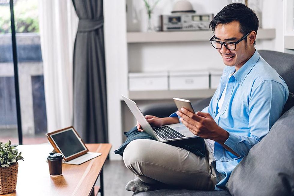 Man on phone and laptop edits his resume while looking for a job