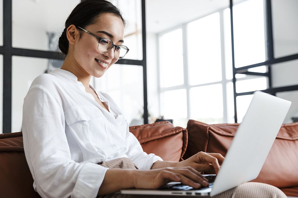 Woman on laptop avoids looking overqualified by only highlighting necessary degrees on her resume