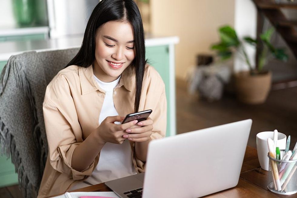 Woman working on phone and laptop adds a certification to her resume